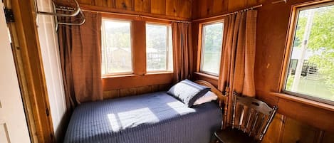 Una habitación pequeña estilo cabaña con una cama individual, una silla y una ventana.