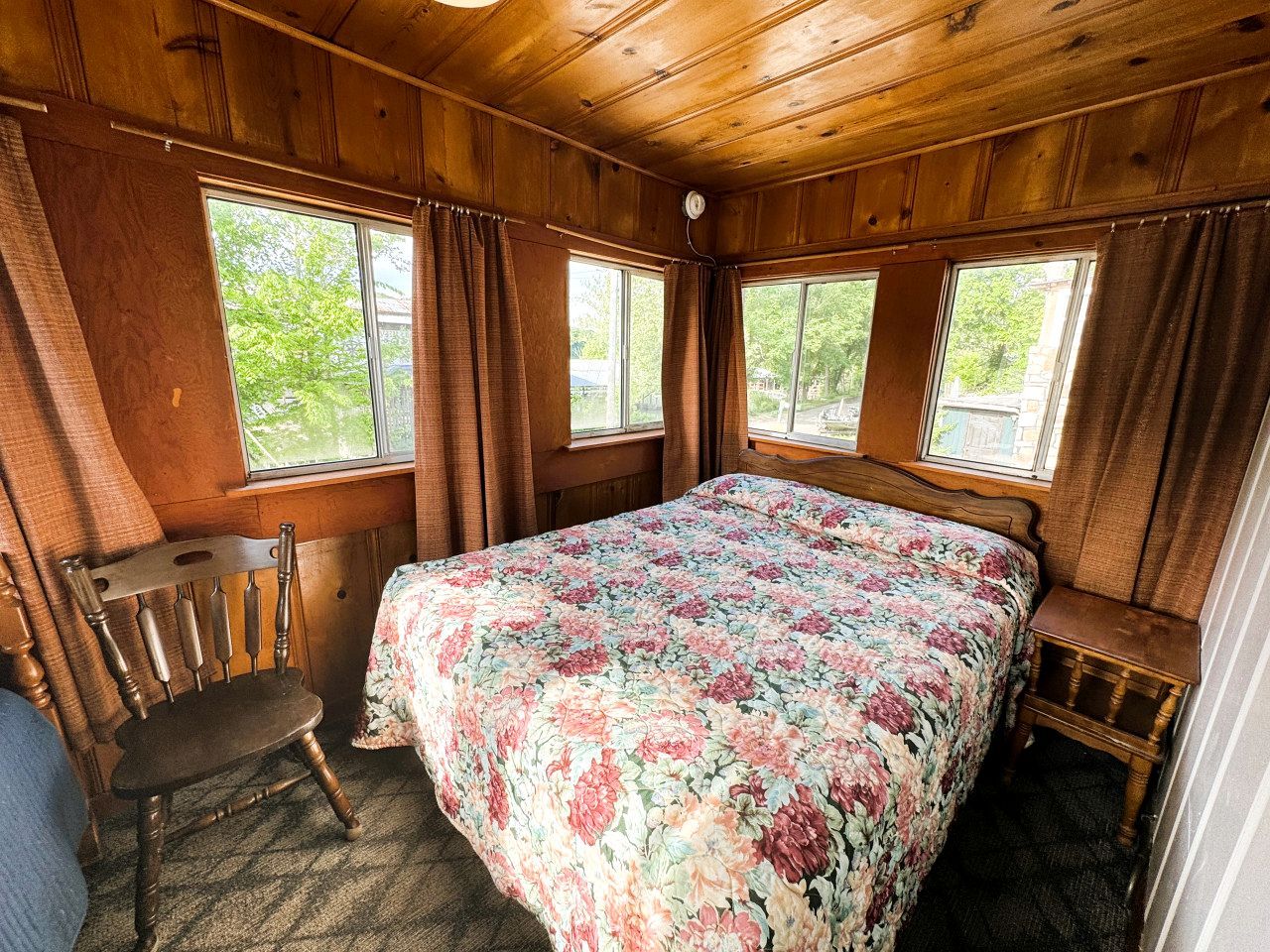 Ein Schlafzimmer einer Holzhütte mit einem Bett, einem Sessel und einem Fenster.