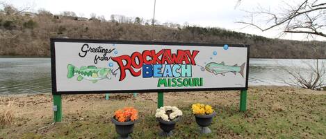 Un letrero con el texto 'Greetings from Rockaway Beach, Missouri' y una ilustración de un pez.