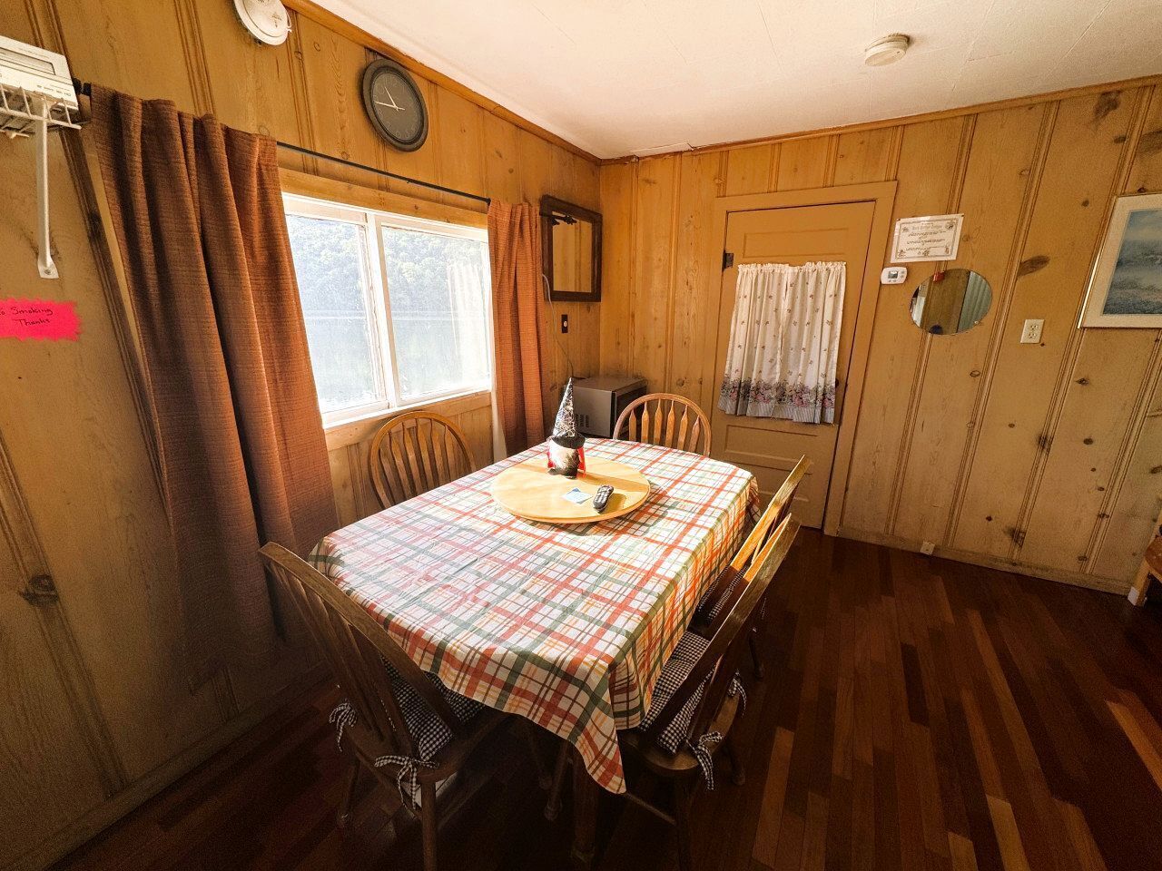 A wooden-paneled room with a table set for two, a clock on the wall, and a door with a sign.