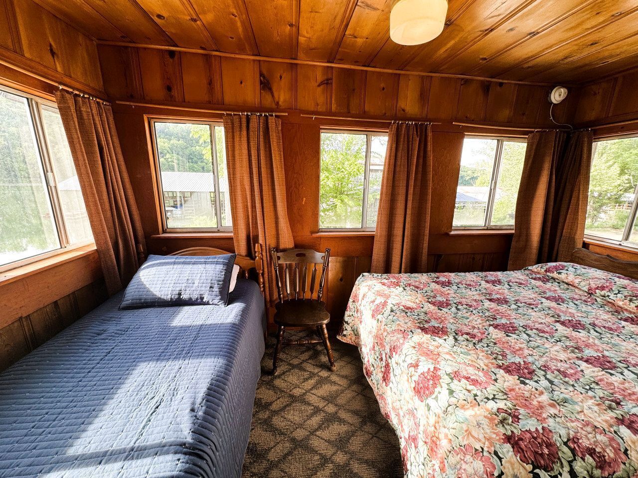A cabin with two beds, a wooden ceiling, and large windows.
