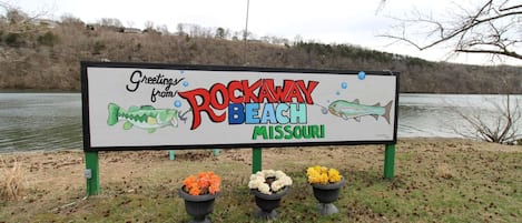 Un letrero con el texto 'Greetings from Rockaway Beach, Missouri' y una ilustración de un pez.