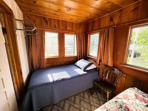Ein kleines Zimmer im Blockhausstil mit einem Bett, einem Sessel und einem Fenster.