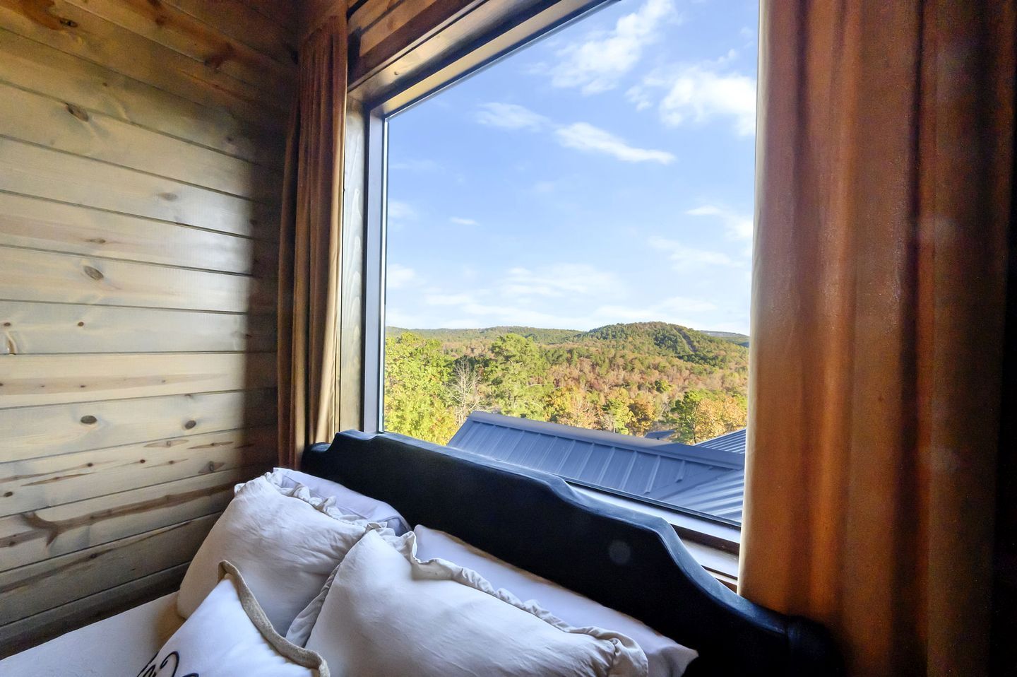 A room with a large window, wooden walls, and a bed with pillows.