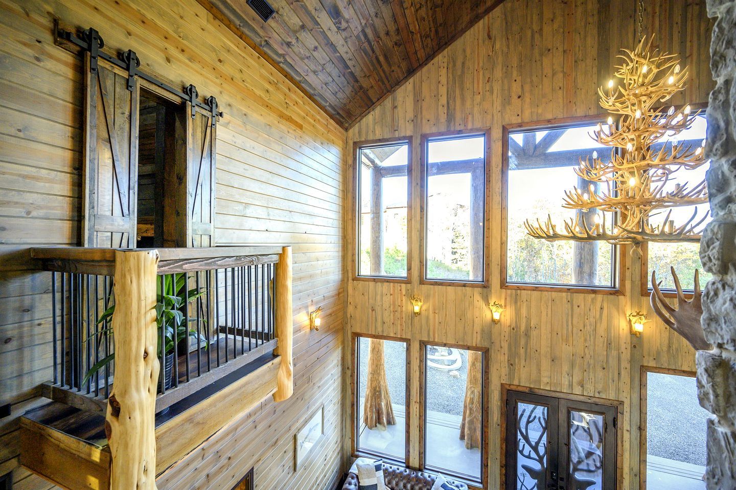 Ein Holzblockbau-Innenraum mit Balkon, großen Fenstern und einem Kronleuchter aus Hirschgeweihen.