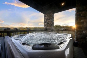 Un bain à remous doté d’une terrasse en bois, de piliers en pierre et offrant une vue sur le paysage.