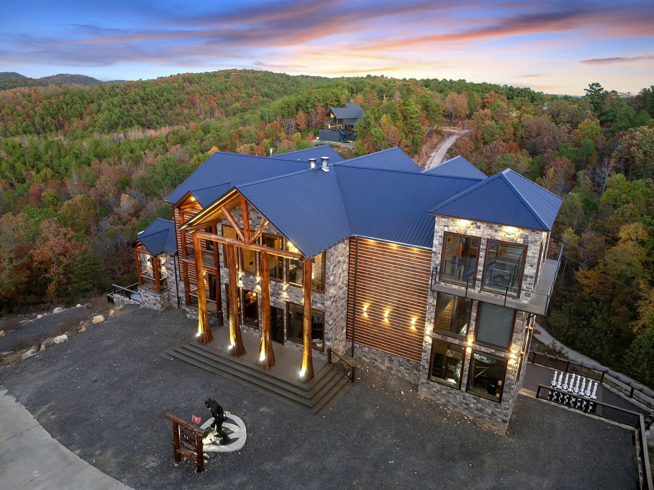 A multi-story lodge with a stone facade, a covered porch, and a view of a forested hillside.