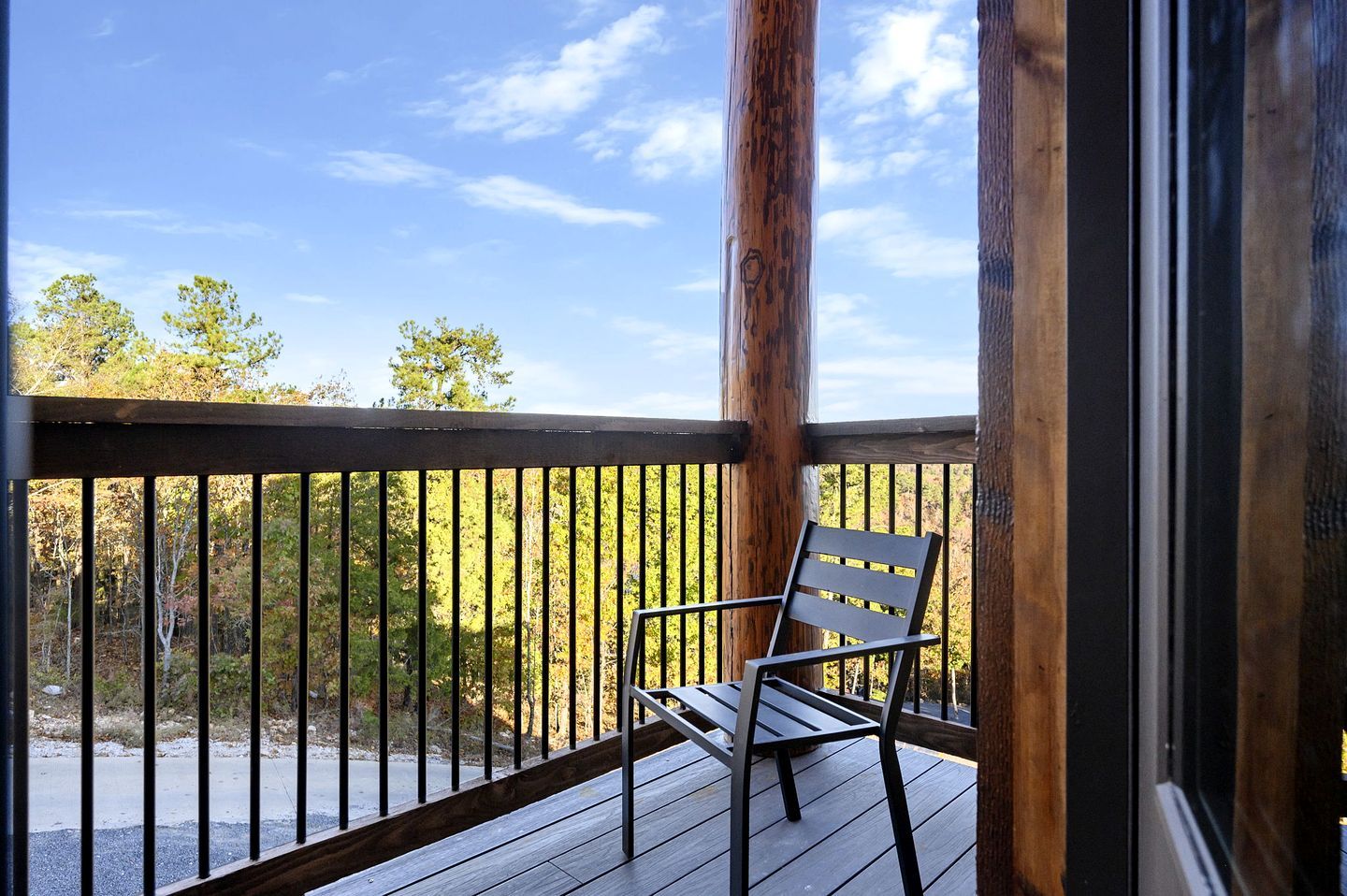A wooden deck with a metal railing, a single chair, and a view of trees and sky.