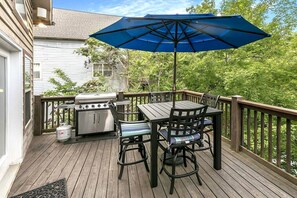 Eine Terrasse mit Grill, Tisch, Stühlen und einem blauen Sonnenschirm.