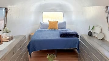Un interior compacto y bien iluminado con una cama, mesitas de noche y una pequeña mesa redonda con una planta.