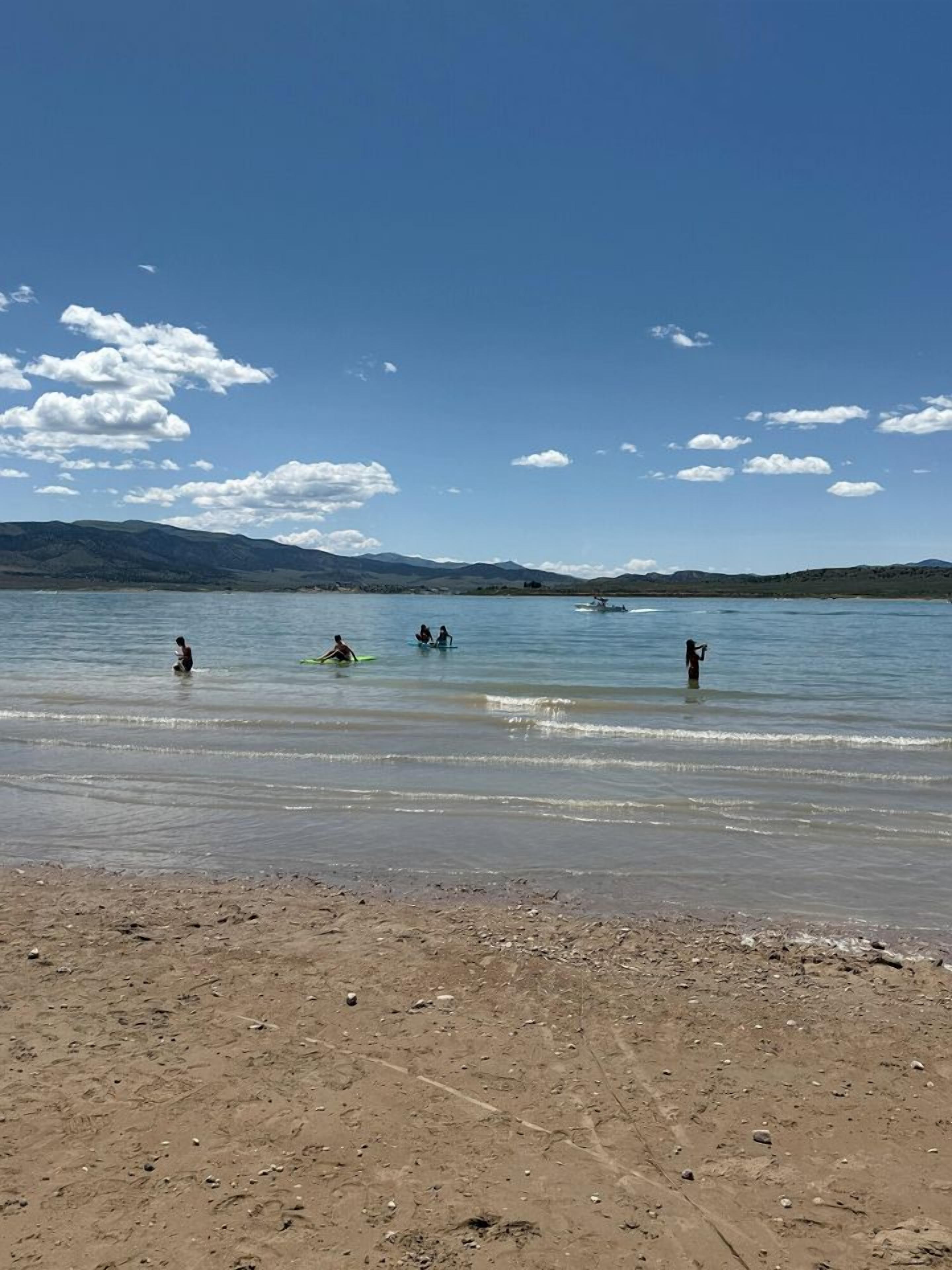 A beach with people in the water, a clear sky, and distant mountains.