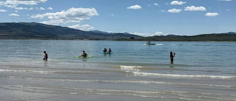 A beach with people in the water, a clear sky, and distant mountains.
