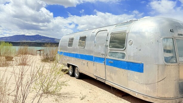 A vintage silver bus parked on a sandy area with a clear sky and mountains in the background. - Beautifully Refurbished Airstream on Yuba Lake for a Unique Getaway in Nature in Utah (Levan)
