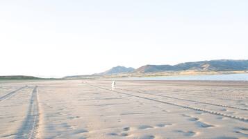 A wide, open sandy area with tire tracks and a distant mountain range.