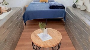 A compact, well-lit interior with a bed, bedside tables, and a small round table with a plant. - Beautifully Refurbished Airstream on Yuba Lake for a Unique Getaway in Nature in Utah (Levan)