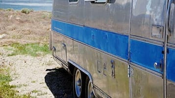 A vintage camper van parked by a lakeside with a clear sky.