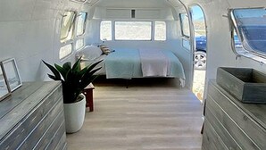 A narrow, elongated interior with a bed, a potted plant, and a bench. - Beautifully Refurbished Airstream on Yuba Lake for a Unique Getaway in Nature in Utah (Levan)