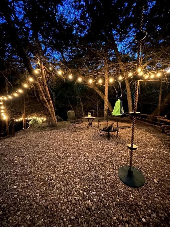 An outdoor area with string lights, a swing, and a fire pit.