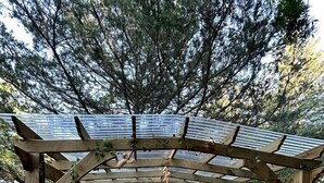 A wooden pergola with a table and chairs underneath, surrounded by gravel. - Unique Jungle-Style Glamping RV with 8-Foot Suspended Tree Tent near Creek Trails in Forestburg, Texas (Forestburg)