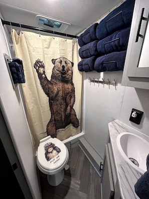 A bathroom with a bear-themed shower curtain, a toilet with a bear illustration, and a stack of towels.