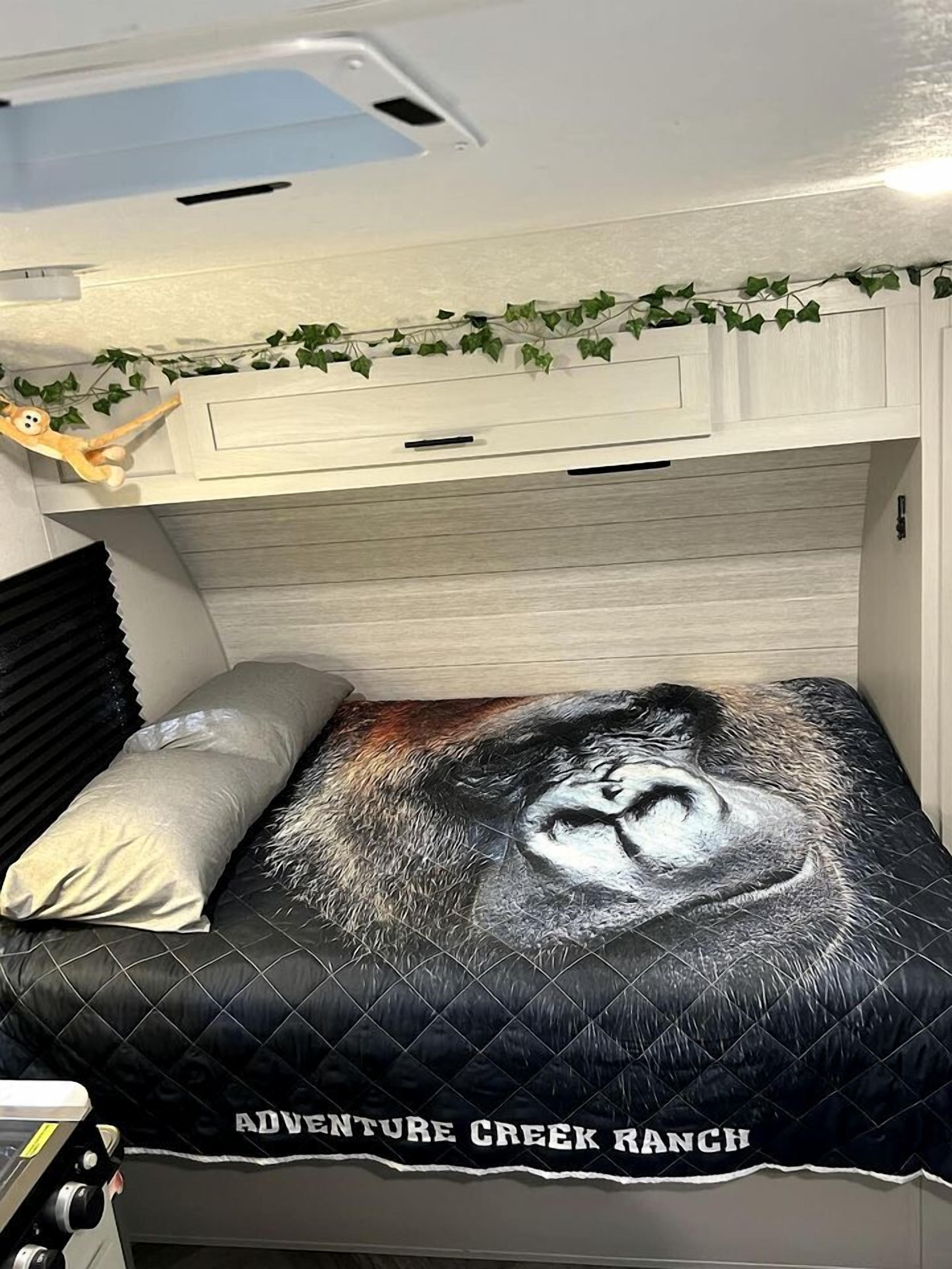 A bed with a quilted cover featuring a face design and the text 'ADVENTURE CREEK RANCH'.