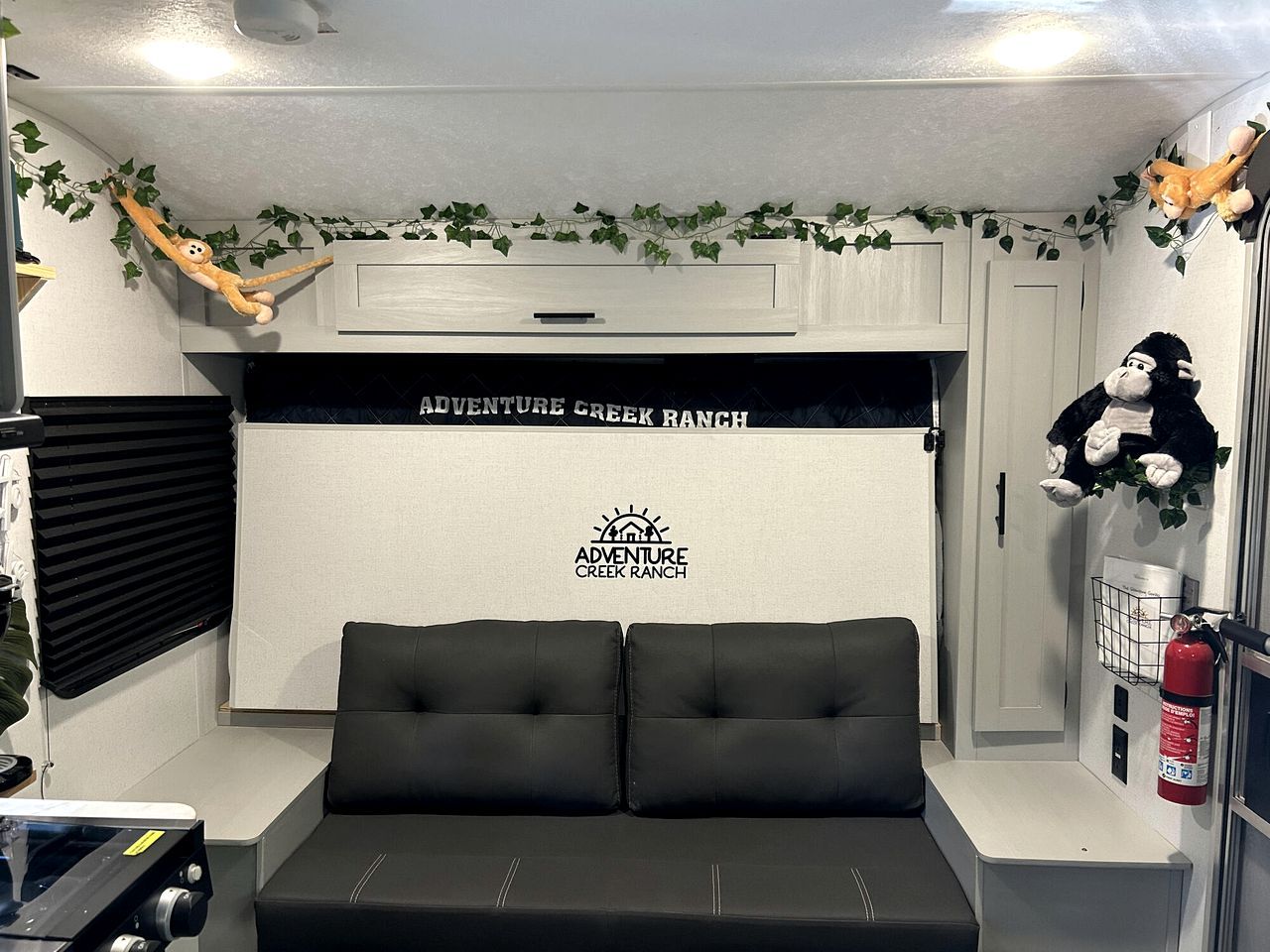 A room with a black sofa, a white wall with 'Adventure Creek Ranch' branding, a window with blinds, and a fire extinguisher.