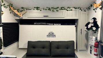 A room with a black sofa, a white wall with 'Adventure Creek Ranch' branding, a window with blinds, and a fire extinguisher.