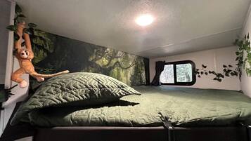 Un lit superposé avec un matelas matelassé vert, un jouet en peluche suspendu et une fenêtre donnant sur des arbres.