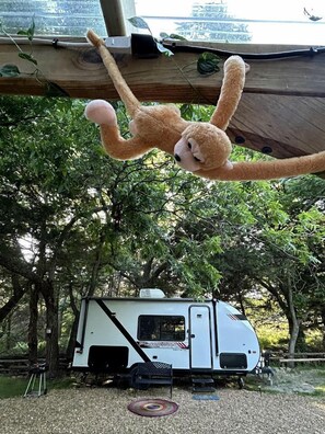 Una caravana estacionada en un área boscosa con un árbol grande y un peluche colgando.