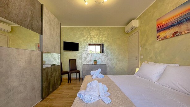 Quarto de hotel com cama, poltrona, escrivaninha e televisão.