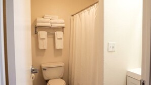 Un baño con inodoro, toallero con toallas dobladas, cortina de ducha y pared blanca.