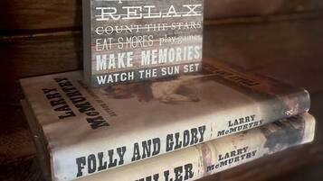 A wooden shelf with a sign listing cabin rules and three books titled 'Folly and Glory,' 'Sin Killer,' and 'Larry McMurtry.'