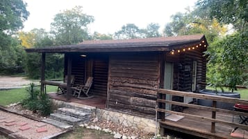 Una cabaña rústica de troncos con un porche, mobiliario exterior y un hogar.