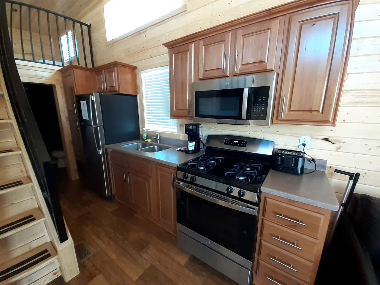 A kitchen with wooden cabinets, a stainless steel refrigerator, a microwave, a stove, and a coffee maker.