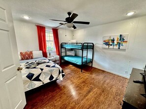 Una habitación con una cama individual, una litera, un ventilador de techo y un cuadro en la pared.