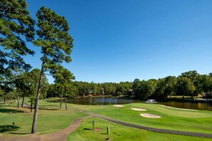 Un campo de golf con un estanque, árboles y cielo despejado.
