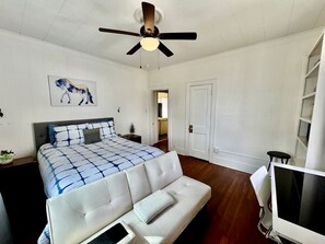 Ein Schlafzimmer mit einem Bett, einem weißen Sofa, einem Deckenventilator, einem Fernseher und einer Tür.