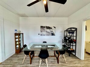 A dining area with a glass table, black chairs, a ceiling fan, a wall-mounted picture, a wooden cabinet, and a black shelving unit. - Spacious Vacation Home Near Trails & Entertainment in Hot Springs, Arkansas (Hot Springs)