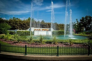 En springvand med vandstråler, omgivet af en velplejet have med et skilt, der siger 'MAGIC SPRINGS'.