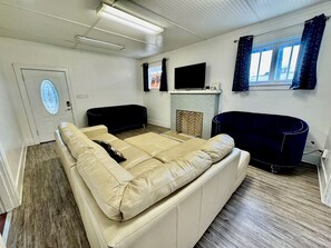 Ein Wohnzimmer mit einem beigen Sofa, einem dunkelblauen Sessel, einem Flachbildfernseher und einem Kamin.