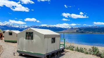 A white tent with a small window, a green ramp, and a view of a lake and mountains.