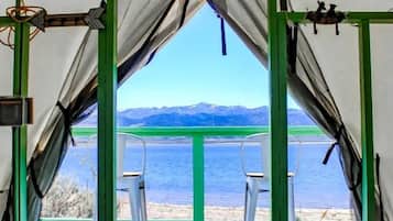 Una carpa con vistas a un lago y montañas, una cama con colcha y una silla afuera.