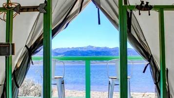 A tent with a view of a lake and mountains, a bed with a quilt, and a chair outside.