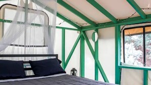 Una cama con dosel, una ventana con vista a árboles y vigas estructurales verdes.