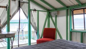 Una habitación tipo tienda de campaña con una cama, una silla roja y una mesa.