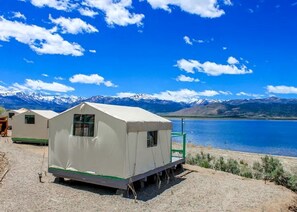 Une tente blanche avec une petite fenêtre, une rampe verte et une vue sur un lac et des montagnes.