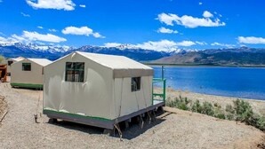 Una carpa blanca con una pequeña ventana, una rampa verde y vistas a un lago y montañas.