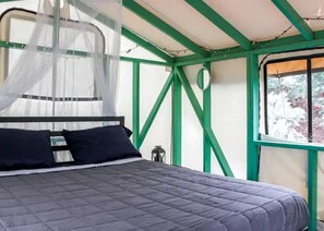 Un lit à baldaquin, une fenêtre donnant sur les arbres et des poutres apparentes de couleur verte.