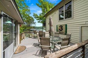 A covered outdoor patio with a table and chairs, a wooden deck, and a view of a lake. - Enormous Cabin Fully Loaded Dock for Water Sports in Tennessee (Rocky Top)