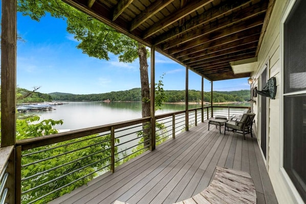 Une terrasse couverte avec vue sur un lac, des meubles en bois et une rambarde.